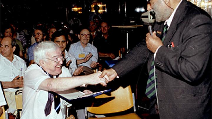 Elias Burstein, the man in the background wearing a light blue shirt and applauding, at an ICTP symposium honoring Stig Lundqvist (left), a former chair of ICTP's Scientific Council, here receiving congratulations from ICTP founder Abdus Salam